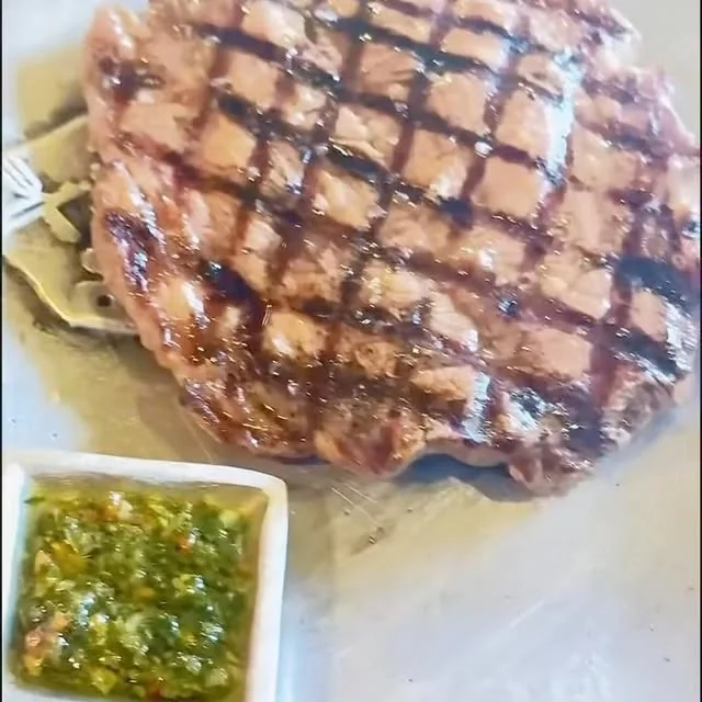 Corte de res con marcas de parrilla, servido con el chimichurri de la casa